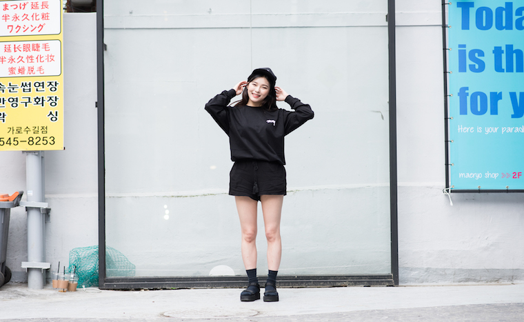 24 year old Korean student Jo Yoo Min smiles candidly wearing a black t-shirt, shorts, and an ivy cap.