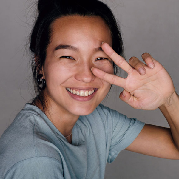 Studio portrait of cheerful black-haired Korean girl gesturing peace sign at camera